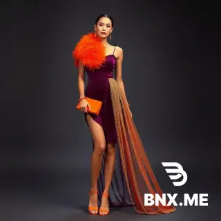 Full-length fashion photoshoot of a woman wearing a short velvet purple slip dress with thin straps, orange flat sandals, orange clutch bag, large orange feather collar and feather bracelets, over a golden sparkling waterfall-like detachable overskirt (resembling a sautoir necklace) that flows down, golden glittering chains attached to the dress straps hanging over shoulders, short golden chain necklace, long golden dangling earrings, carnival themed, festive Rio de Janeiro vibe, studio photography, dramatic lighting, vibrant colors, elegant yet playful, 8k, photorealistic --ar 3:4 --v 6