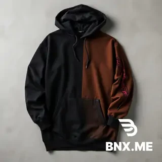 "High-quality studio product shot of a heavyweight, oversized streetwear hoodie laid flat on a neutral grey concrete background. The hoodie features an asymmetrical, vertical color-blocked design: the left side and most of the front are deep matte black, while a contrasting vertical panel on the right side and the right sleeve are a rich chocolate brown. A key detail is a long vertical slit or distressed 'tear' on the outer forearm of the brown sleeve, revealing a secondary inner layer of bright red fabric with an intricate black graphic or paisley-style print. The hoodie has a large front kangaroo pocket, dropped shoulders, and a thick, structured double-layered hood without drawstrings."